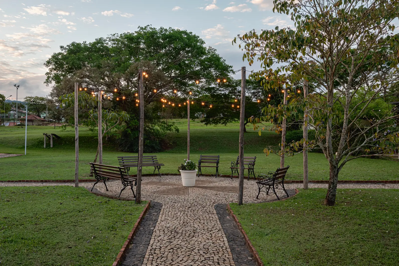 Jardim com varal de luzes, caminho de pedra portuguesa e bancos